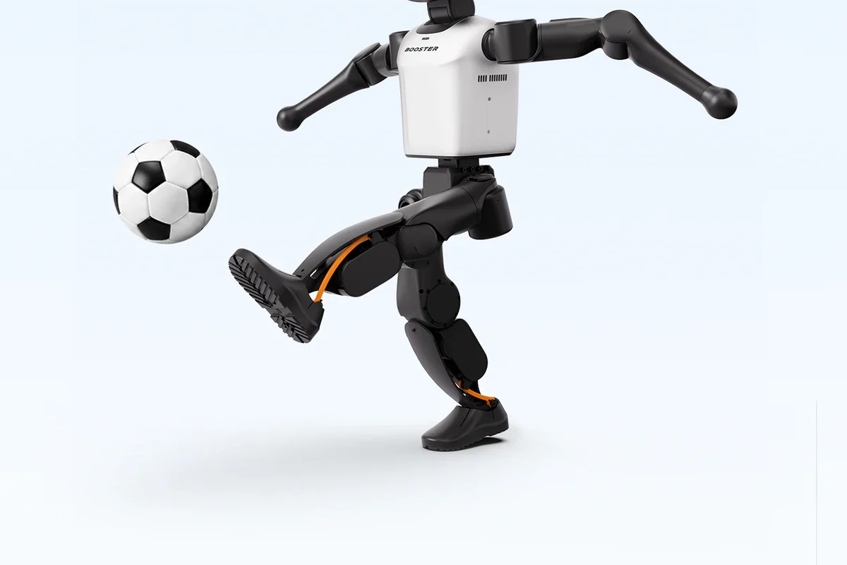 Robot humanoïde Booster Robotics K1 en position de frappe d'un ballon de football, portant la marque BOOSTER sur le torse