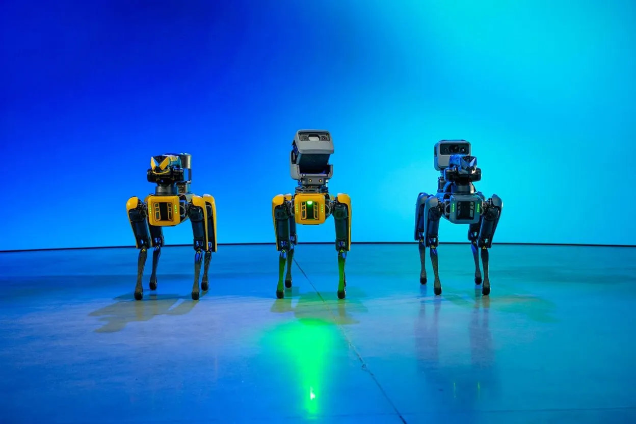Trois robots quadrupèdes Spot alignés sur sol plat avec leurs capteurs et module central caractéristiques, deux à structure jaune et noire, un à structure bleue et noire
