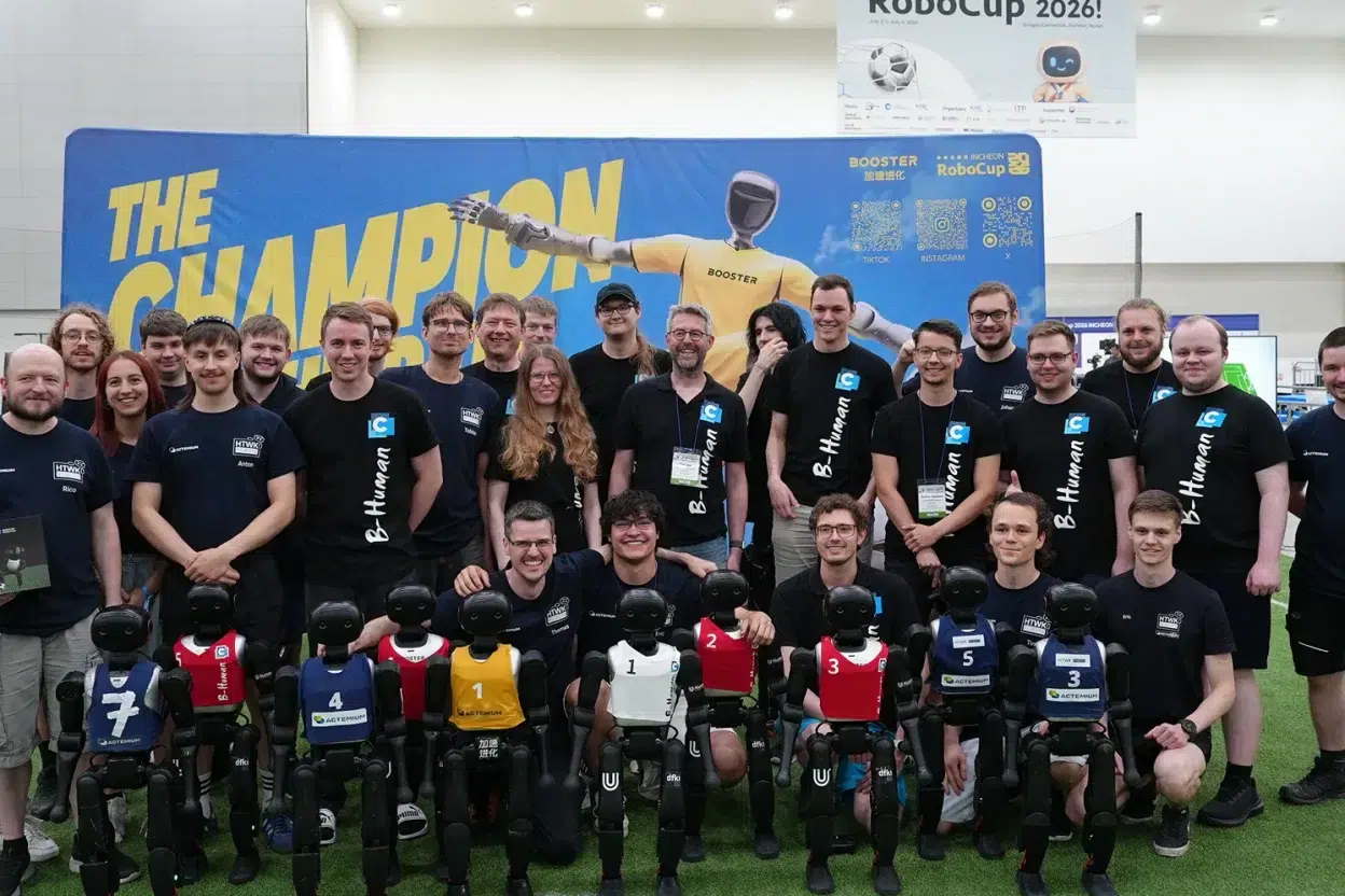 Équipe de participants à la RoboCup 2026 posant avec neuf robots humanoïdes Booster alignés devant une bannière « THE CHAMPION »