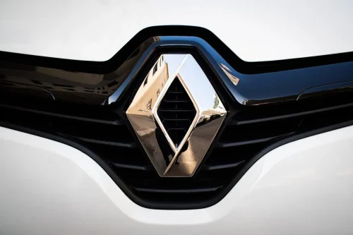 Gros plan sur le logo Renault d'un véhicule garé, reflet d'un immeuble visible dans le chrome