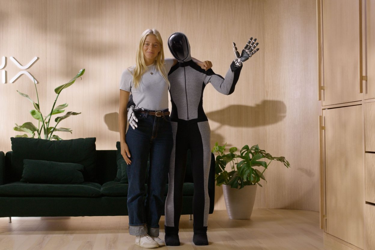 Humanoider Roboter NEO von 1X Technologies neben einer Person in einer Wohnung mit Sofa und Pflanzen