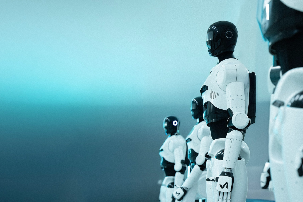 Mehrere weiße humanoide Roboter mit schwarzen Köpfen, in einer Reihe aufgestellt und von hinten zu sehen, in einer blau getönten Umgebung.