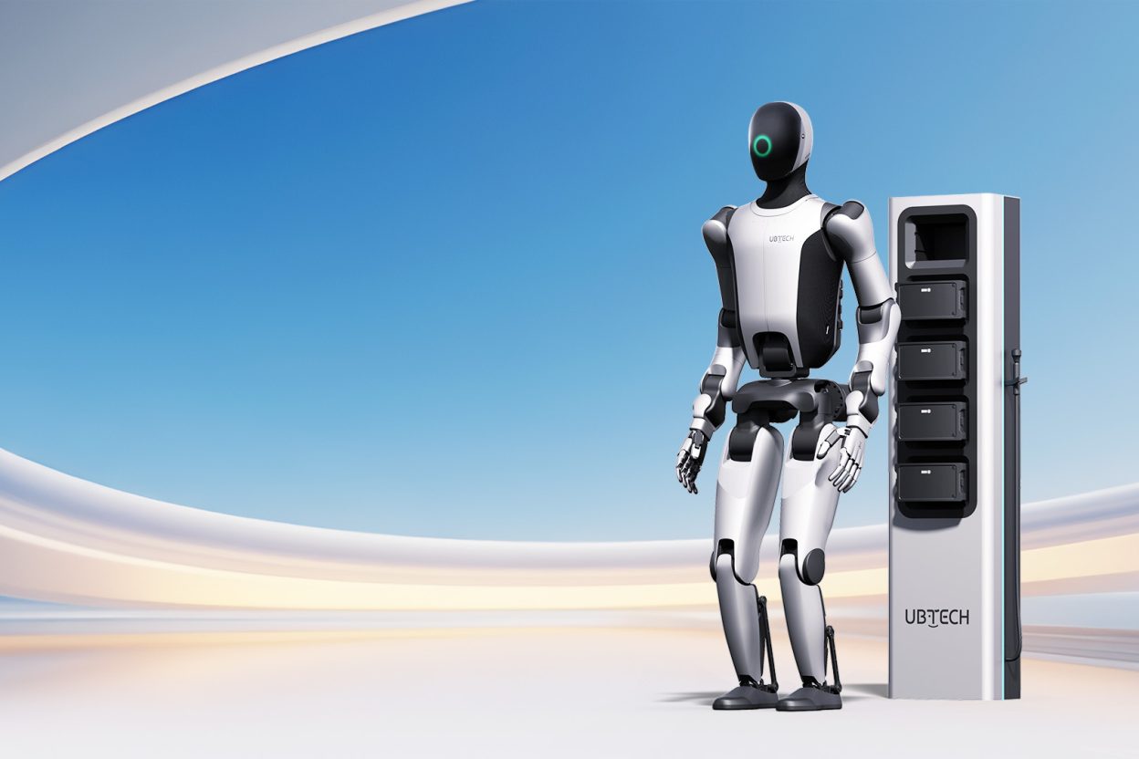 Robot humanoïde en pied à côté d'une station de recharge modulaire avec écran lumineux vert.